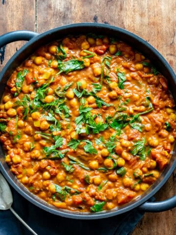 A cast iron dish of chickpea curry on a wooden table.