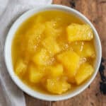 Close up of a bowl of pineapple sauce on a wooden table.