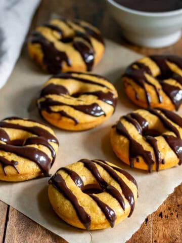 Baked pumpkin donuts with chocolate glaze on baking paper on a table.