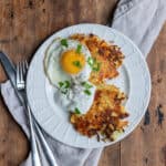 A plate with two cabbage fritters, a fried egg and a dollop of sour cream.