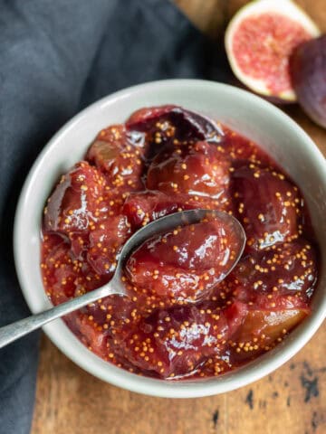 Wooden table with a bowl of fig compote next to a fresh fig.