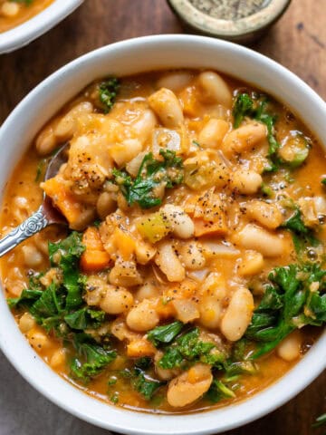 Close up of a spoon in a bowl of kale and white bean soup.