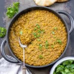 Looking down at a table with a serving dish of Persian lentils with a spoon in it, next to flatbreads and a dish of wilted spinach.