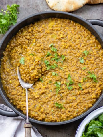 Looking down at a table with a serving dish of Persian lentils with a spoon in it, next to flatbreads and a dish of wilted spinach.