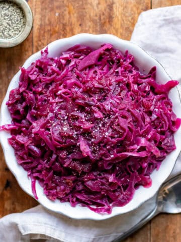 Looking down at a serving dish of braised red cabbage on a wooden table.