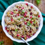 A serving dish of Christmas rice with seasonings, dried cranberries, pistachios and pomegranate seeds.