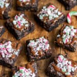 Wooden table with peppermint brownies topped with melted chocolate and crushed candy canes.