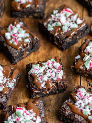 Wooden table with peppermint brownies topped with melted chocolate and crushed candy canes.