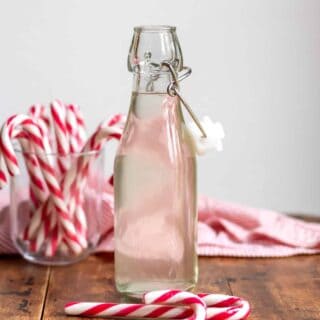 A bottle of peppermint syrup on a wooden table next to candy canes.