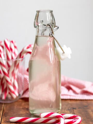 A bottle of peppermint syrup on a wooden table next to candy canes.