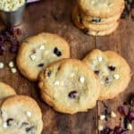A wooden table with white chocolate chip dried cranberry cookies scattered on it.
