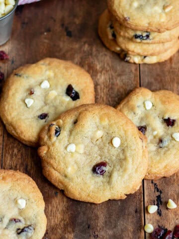 A wooden table with white chocolate chip dried cranberry cookies scattered on it.