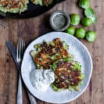 A wooden table with a plate with two brussels sprout fritters next to a knife and fork.