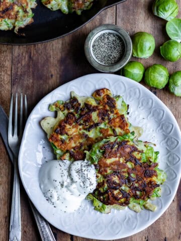 A wooden table with a plate with two brussels sprout fritters next to a knife and fork.