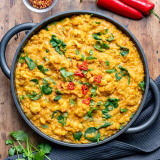 Wooden table with a serving dish of cauliflower and lentil curry.