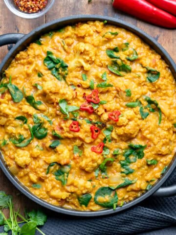 Wooden table with a serving dish of cauliflower and lentil curry.