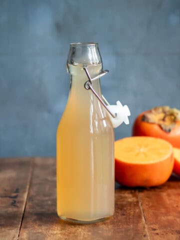 A bottle of persimmon syrup on a table in front of cut persimmons.