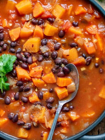 Close up of a spoon in a serving dish of sweet potato black bean soup.