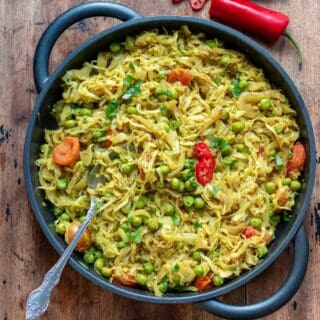 Wooden table with a serving dish of pea and cabbage curry.