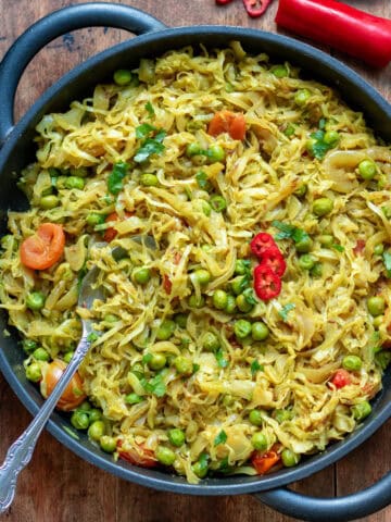 Wooden table with a serving dish of pea and cabbage curry.