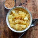 A wooden table with a dish of apple compote and a small dish of cinnamon.