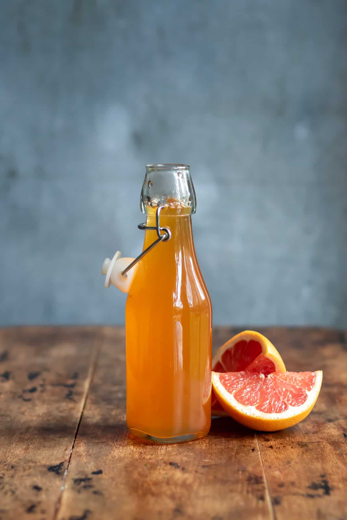 Wooden table with a glass bottle of grapefruit syrup next to slices of pink grapefruit.