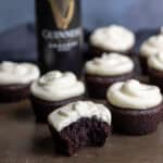 Side view of Guinness chocolate cupcakes topped with cream cheese frosting, with one in front with a bite out.