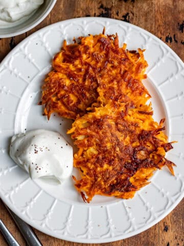 Close up of two sweet potato fritters on a plate on a wooden table.