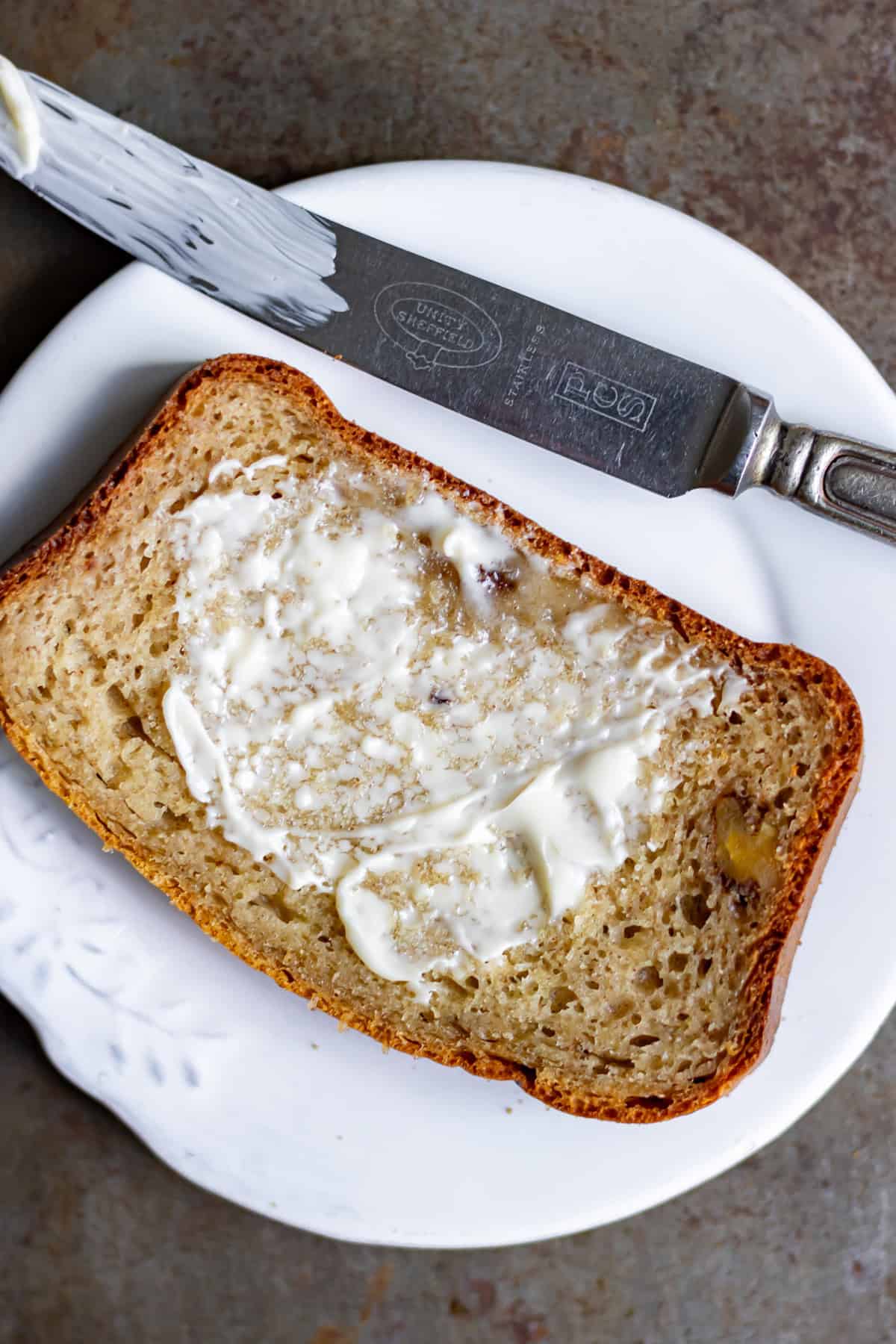 Looking down at a slice of cottage cheese banana bread spread with butter on a plate.