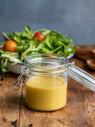 Wooden table with a jar of maple dijon dressing in front of a bowl of salad.