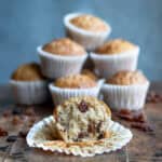 Side view of a table with a raisin muffin with a bite out in front of a pile of muffins.