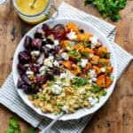 Looking down at a table with a serving dish of roasted beetroot and sweet potato salad with couscous.