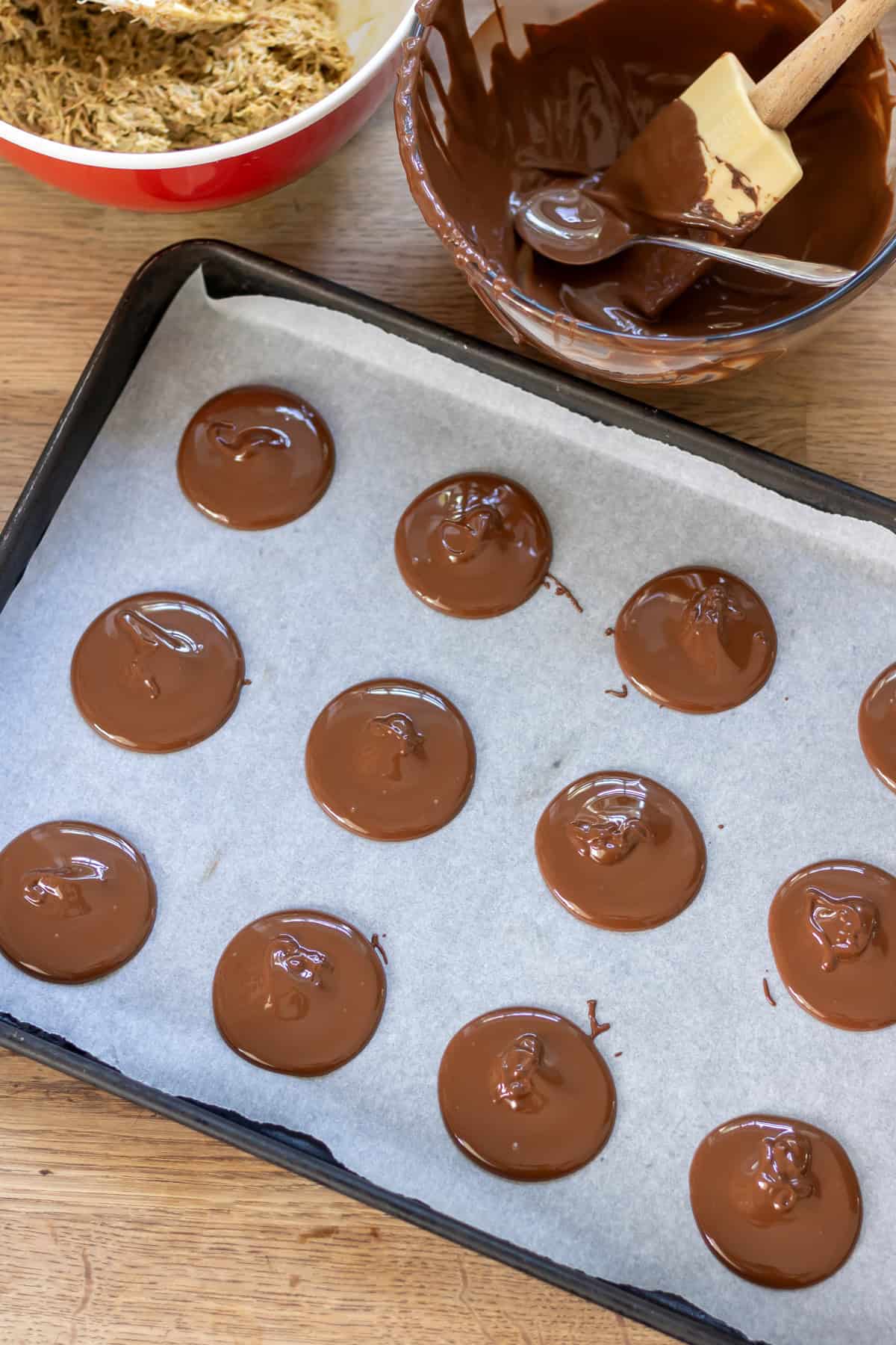 Spooning small discs of melted chocolate onto a baking tray lined with parchment paper.