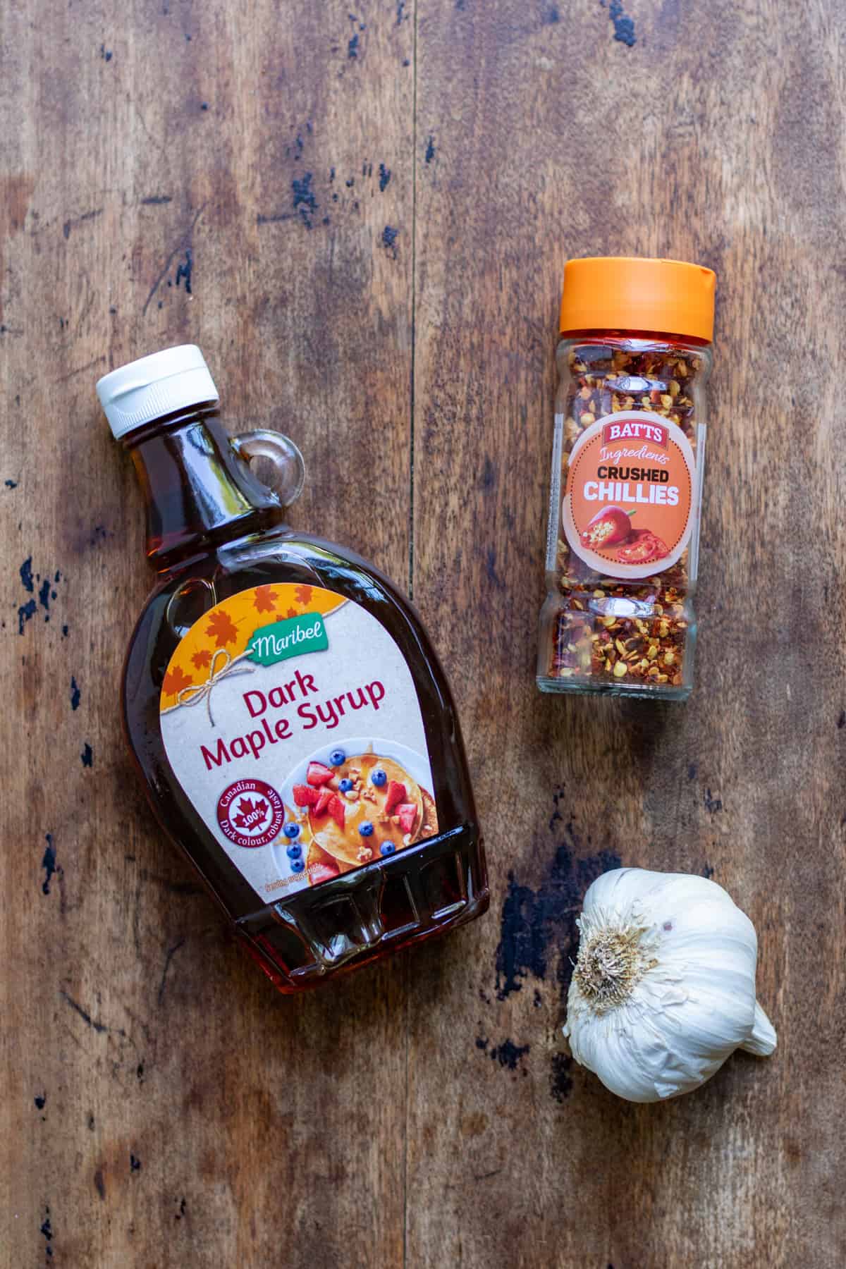 Maple syrup, chili flakes and garlic on a table.