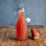 A wooden table with a glass bottle of rhubarb simple syrup.