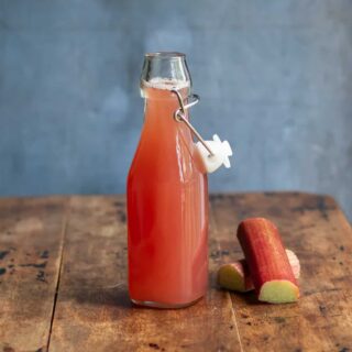 A wooden table with a glass bottle of rhubarb simple syrup.
