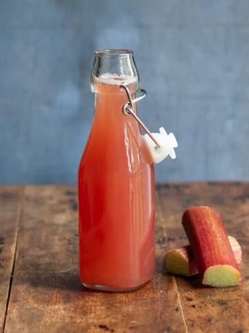 A wooden table with a glass bottle of rhubarb simple syrup.