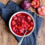 A bowl of plum compote and plums next to it.