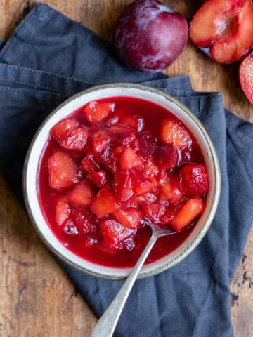 A bowl of plum compote and plums next to it.