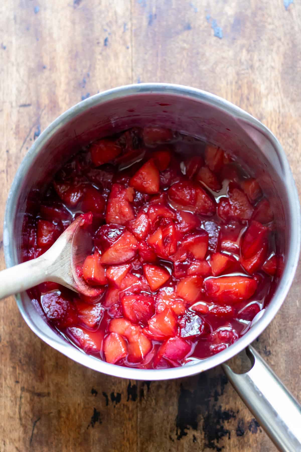 A saucepan with the cooked plum compote, plus a wooden spoon.