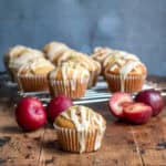 Side view of plum muffins on a wooden table next to fresh plums.