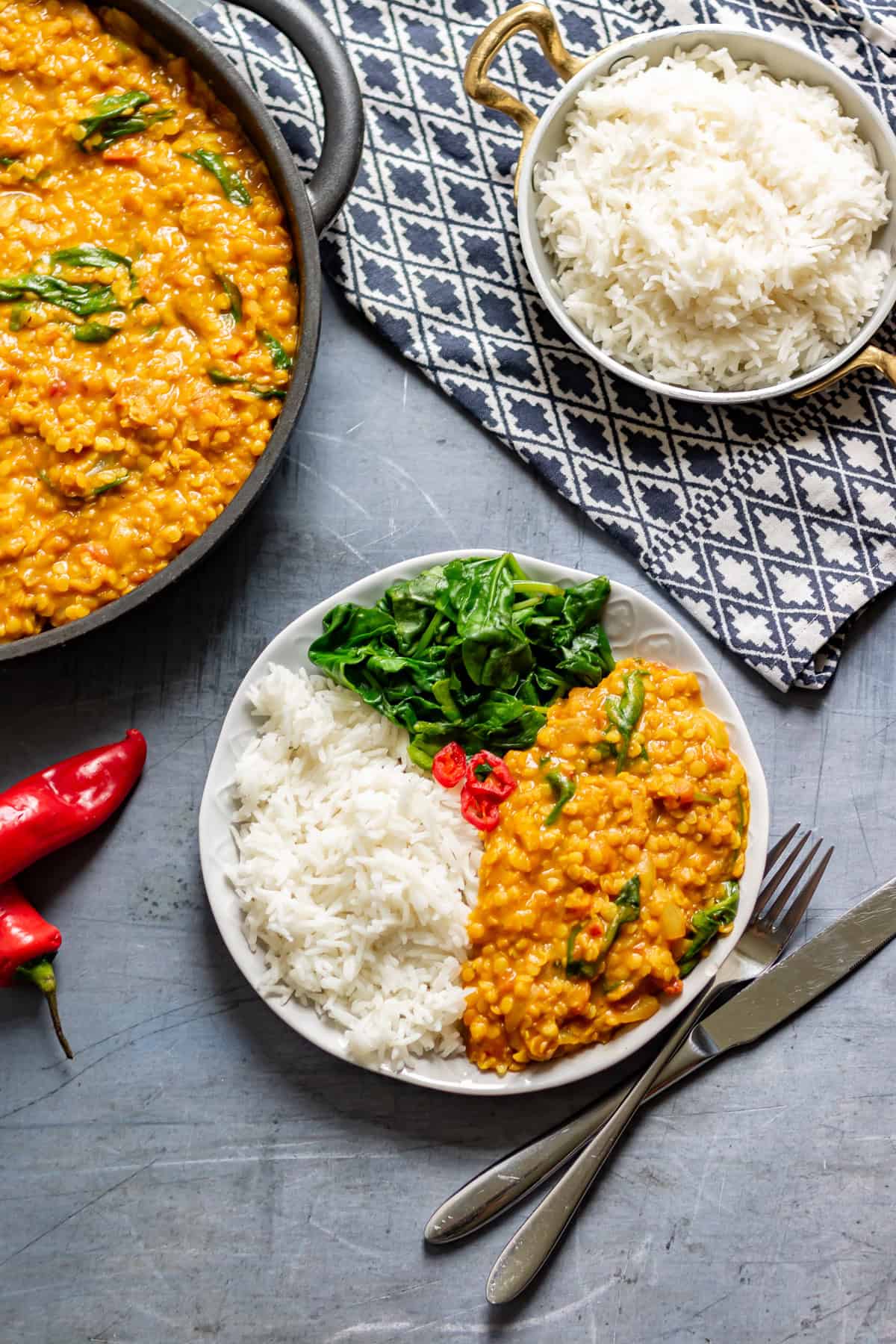 Table with a plate divided into three: rice, red lentil dahl, wilted spinach.