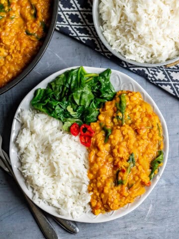 Close up of a plate of red lentil dahl with rice and spinach.