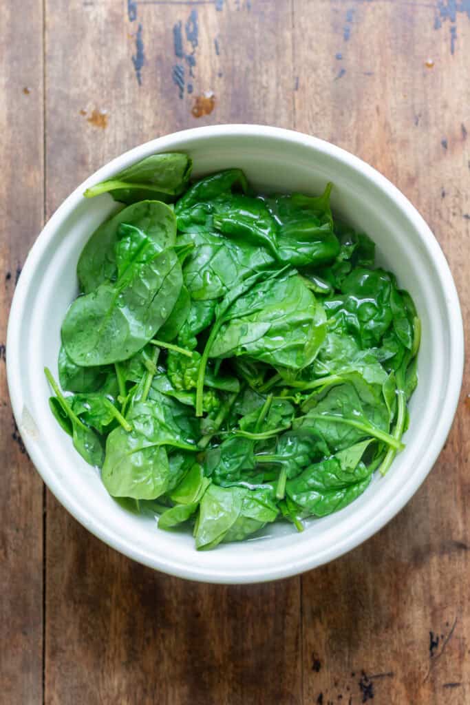 Spinach wilting in a bowl of boiling water.