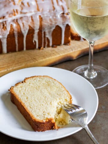 A slice of white wine cake with a glass of white wine.