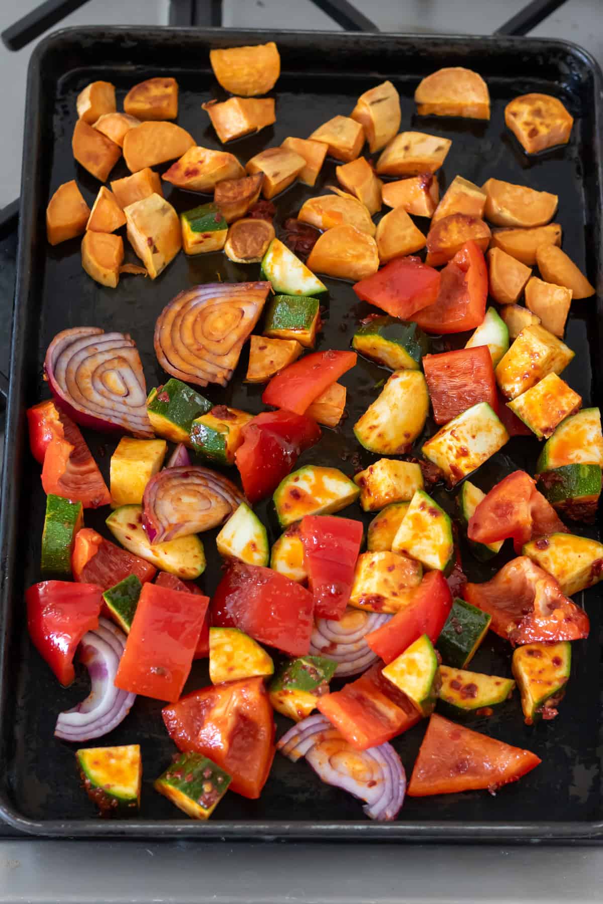 Harissa vegetables added to the baking sheet with partially roasted sweet potatoes.