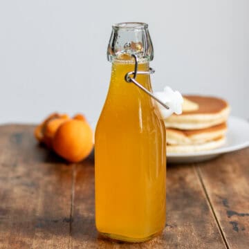 Bottle of apricot syrup on a table in front of pancakes.
