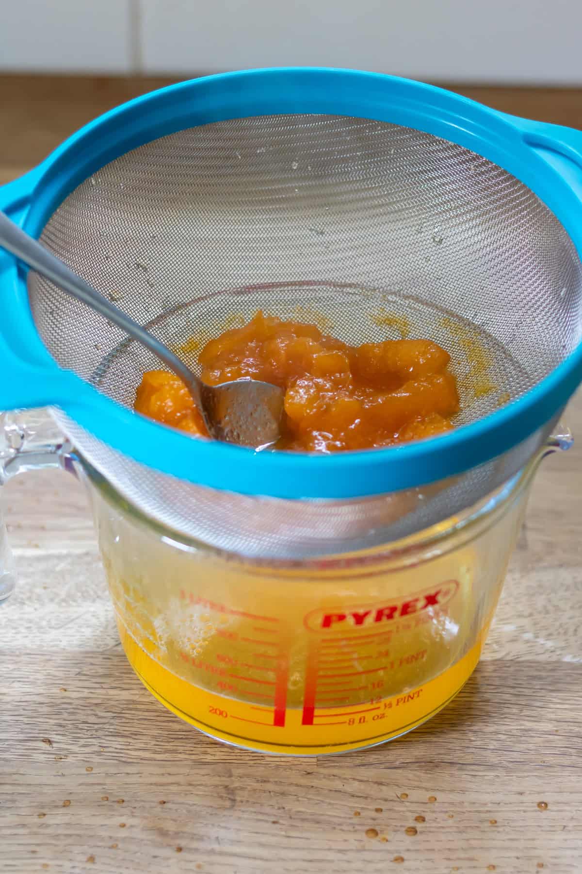 Straining the apricot syrup from the cooked apricots in a strainer over a jug.