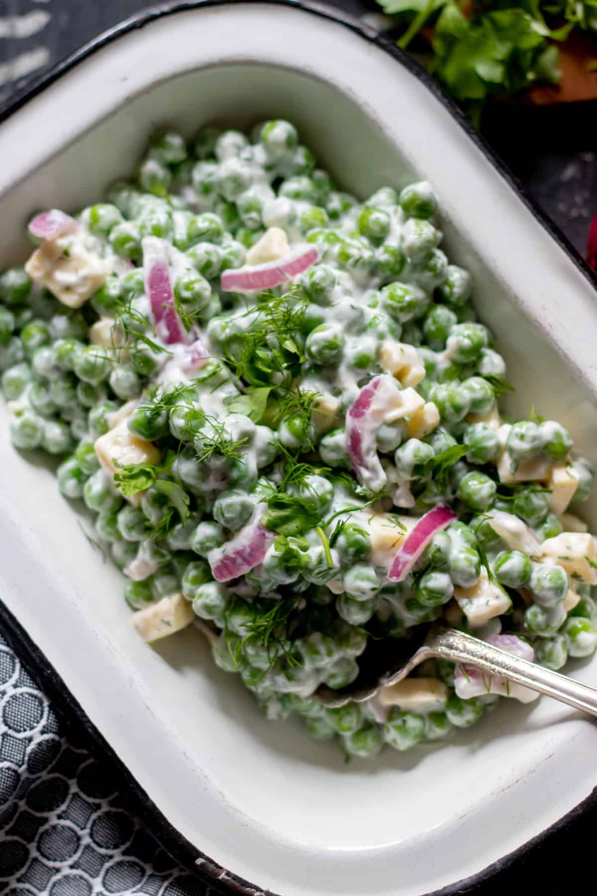 White dish full of pea salad topped with dill.