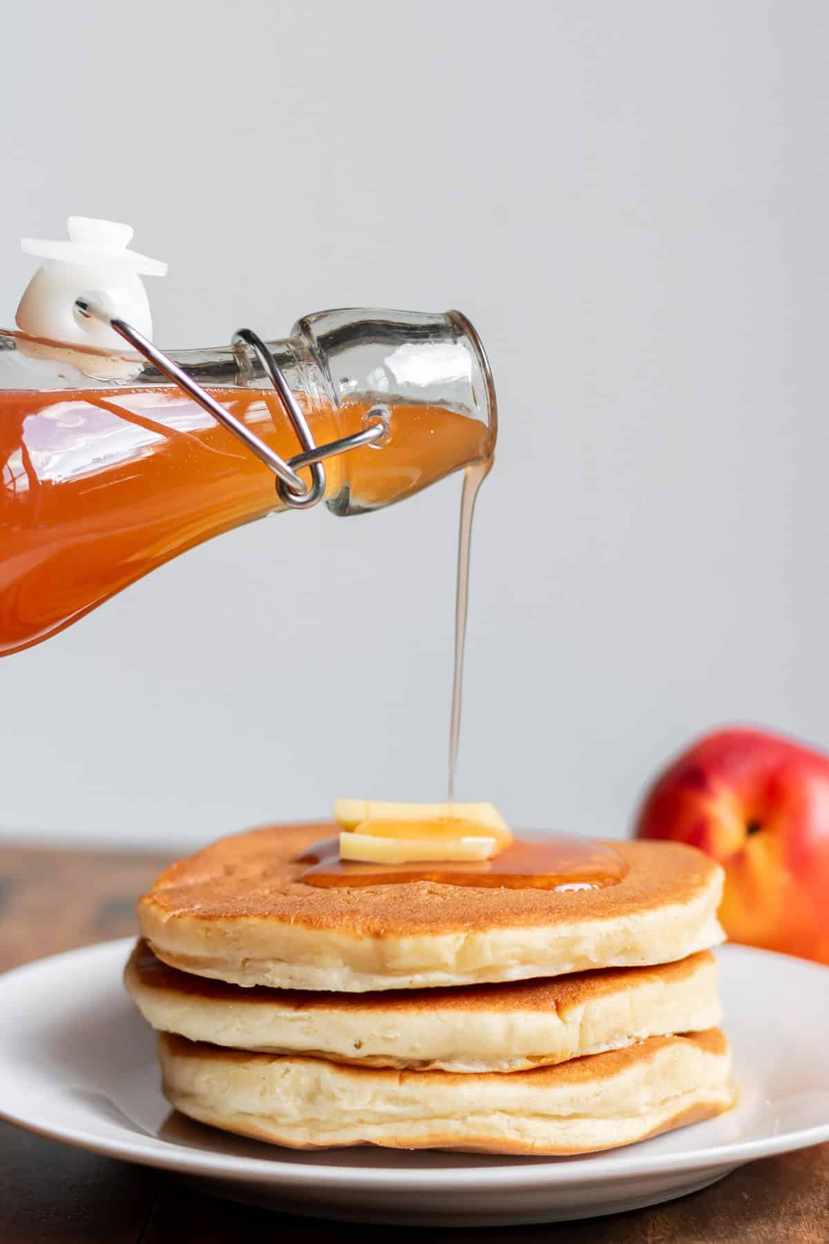Pouring nectarine simple syrup over a stack of pancakes.